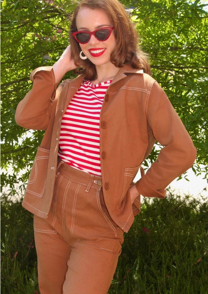 Model wearing 1950s reproduction denim jeans in a toasty cashew brown color with ultra high waist, double brass metal side buttons and a sturdy metal zipper hidden in the left front pocket, full size belt loops, sharp white contrasting stitching, loop stitch detail on the back pockets, and deep front pockets