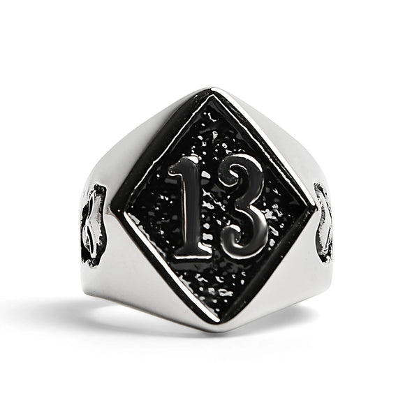 Shiny stainless steel signet style ring depicting the number 13 inside of a diamond shape on the top of the ring with a small skull on either side. Shown from the front 