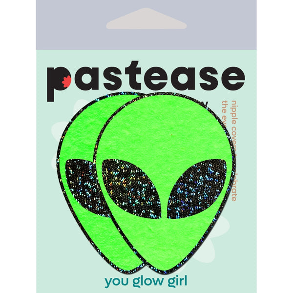 A pair of neon green alien head shaped pasties with black glitter eyes shown in their packaging