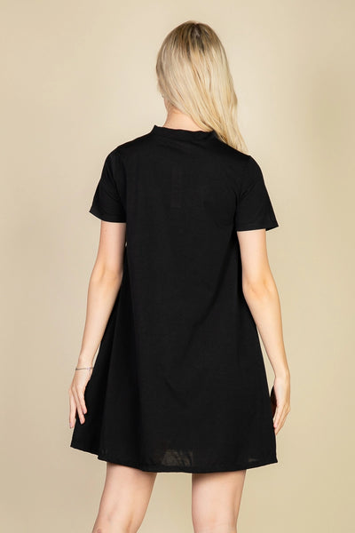 Model wearing a black short sleeved a-line t-shirt mini dress with a high collar. Shown from the back