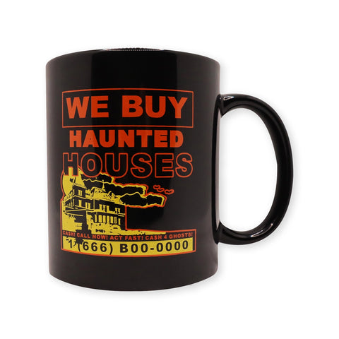 A black ceramic mug with a printed image of a haunted house in orange and red with the caption “WE BUY HAUNTED HOUSES” above. Underneath is the subtitle “CA$H! CALL NOW! ACT FAST! CASH FOR GHOSTS! 1 (666) B00-0000”