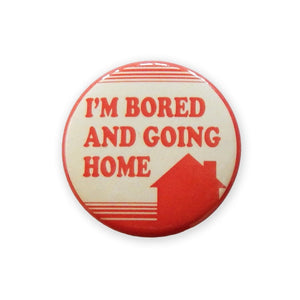 A pinback button with an image of a house surrounded by horizontal red lines on a cream background with the message I’M BORED AND GOING HOME”