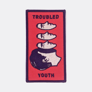 Rectangular red embroidered patch with a navy blue border with an illustration of a man’s face floating away from the rest of his head. The message “TROUBLED YOUTH” is written in matching navy blue capital letters