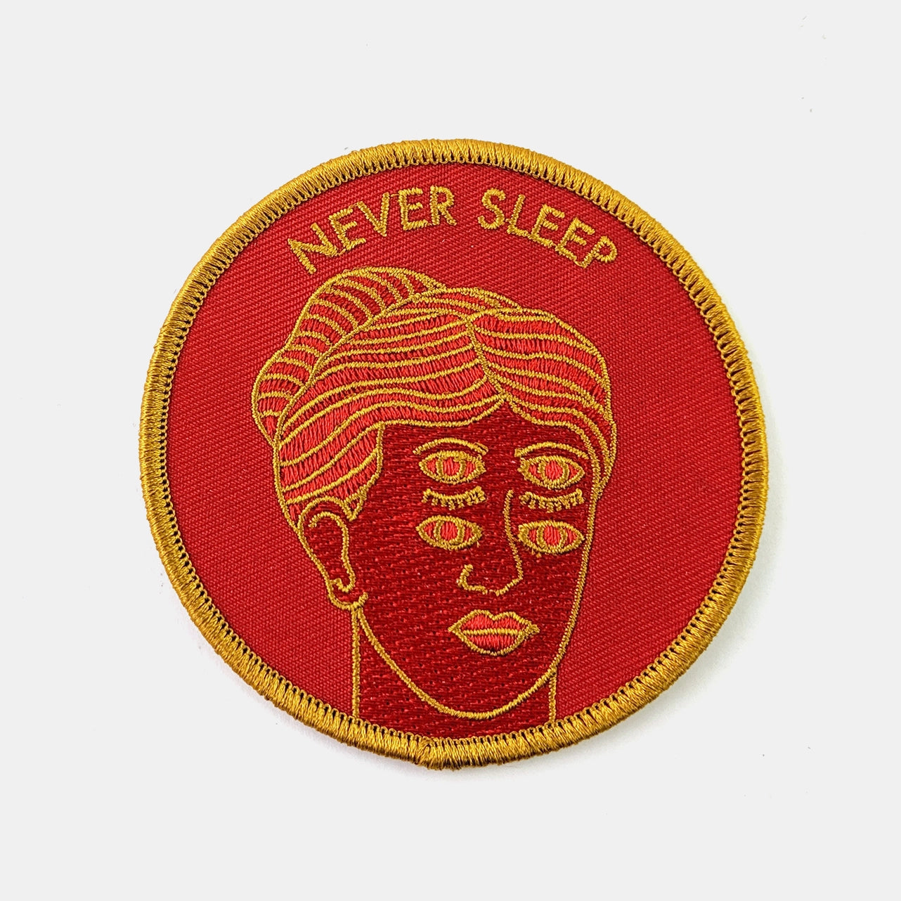 Round red orange embroidered patch with a mustard border and and illustration of a woman with three sets of eyes, two open and one set closed. In mustard outlines and deep red details