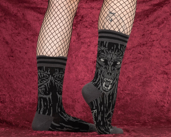  black and grey illustration of a demon with large matching pentagrams on soft black stretch cotton blend crew socks. Worn by a model over black fishnet tights on a red velvet background 