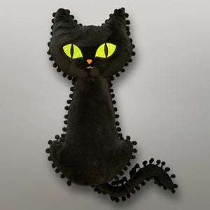 Plush pillow in the shape of a black cat with large bright green eyes, tail, and a black pom-pom trim