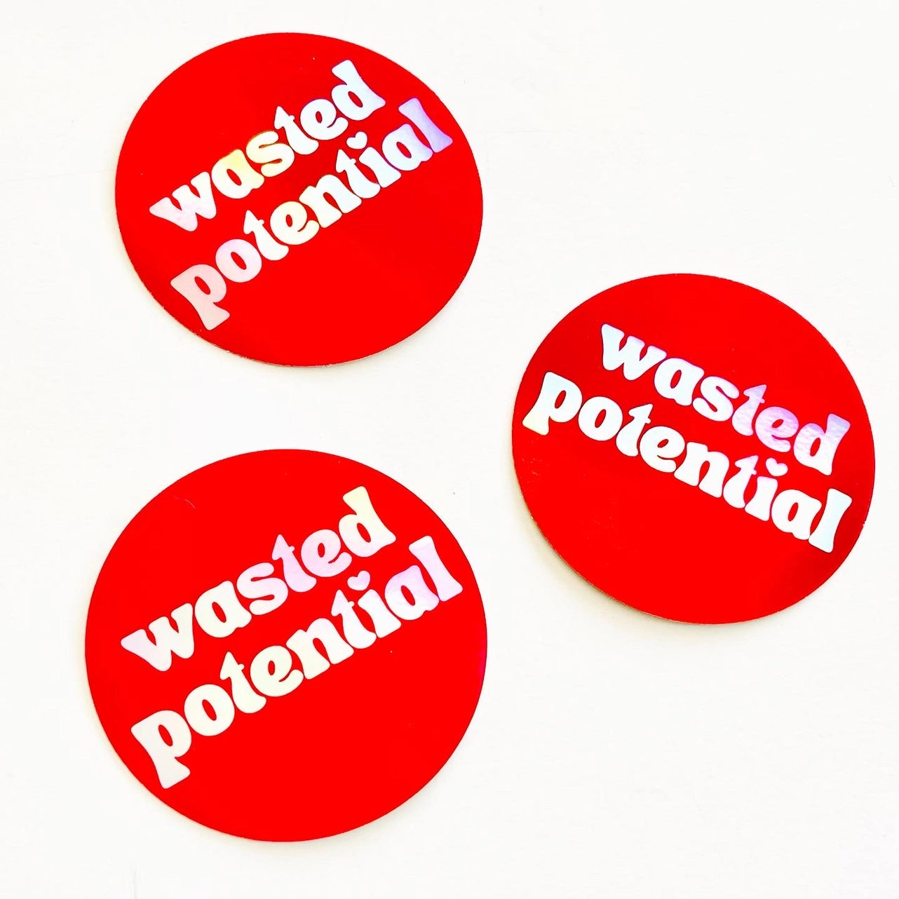 3” round holographic sticker with the phrase “wasted potential” written in lower case holographic letters with a heart shaped dotted letter I. On a bright red background 