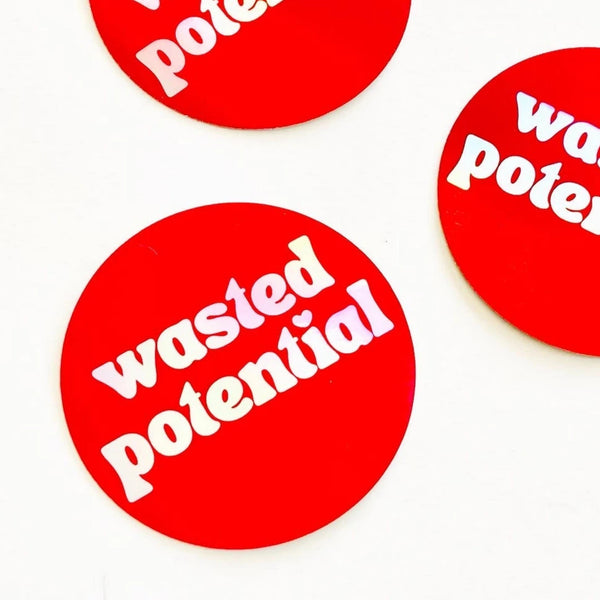 3” round holographic sticker with the phrase “wasted potential” written in lower case holographic letters with a heart shaped dotted letter I. On a bright red background 