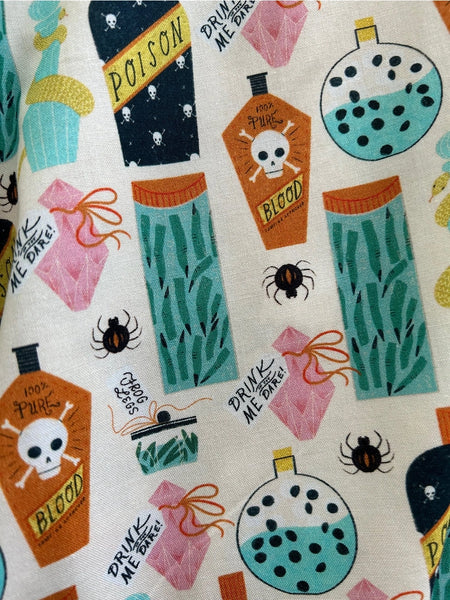 A cotton skater style skirt with an all over pattern of bottles of poison, blood, frog legs, black widow spiders, and witches fingers in shades of orange, bright blue, pink, and black on a light beige background. Pattern shown in close up shot 