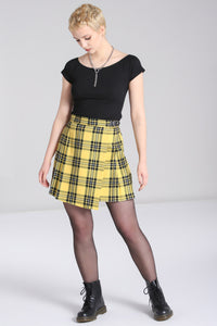 Model wearing a black and yellow tartan print pleated miniskirt with a faux wrap detail in the front. It has a black faux leather strap at the left hip of the waistband with a shiny silver heart shaped buckle. Shown from the front