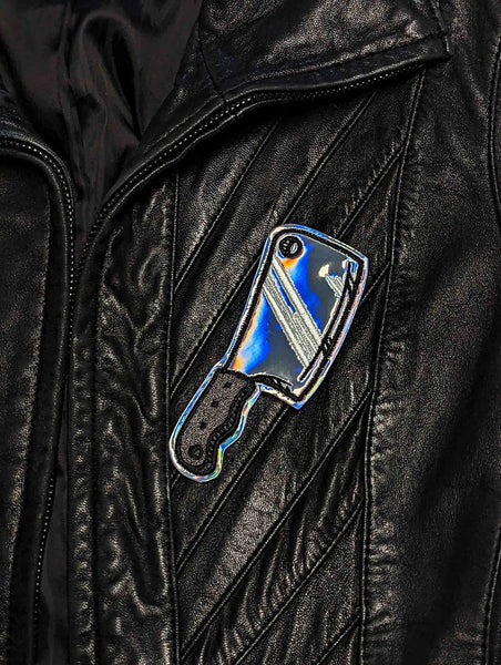 Embroidered patch in the shape of a cleaver with silver holographic vinyl for the blade and a grey and black embroidered handle. Shown on a leather jacket 