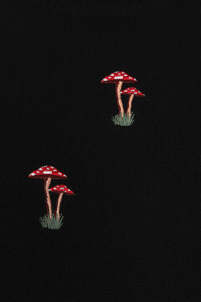Black elbow length sleeved turtleneck sweater with ribbed neck and cuffs. Embroidered toadstool mushrooms in red, white, and brown shown in close up