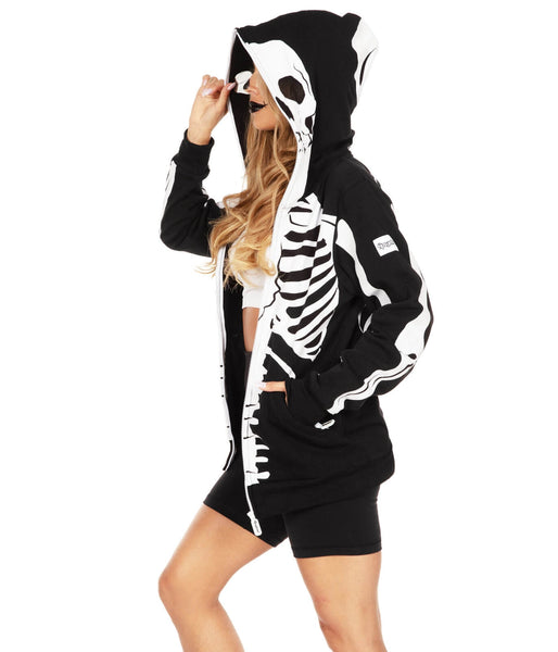 Female model wearing a black fleece lined hooded sweatshirt with an all-over anatomical skeleton screen printed design. Shown unzipped and seen from the side