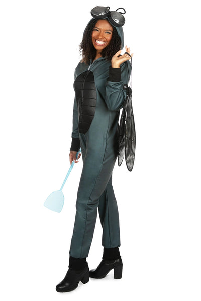 Female model wearing a polyester unisex fly costume jumpsuit. It is dark grey with a black thorax detail on the center of the stomach and has an oversized hood with silver lamé eyes and posable antennae. Shown with hood up, holding fly swatter and pair of wings. Shown from a 3/4 angle