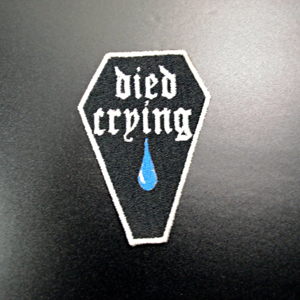 “ died crying” in a gothic font with a big old blue teardrop on an embroidered black coffin shaped patch with white border