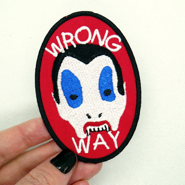 Oval shaped red cotton twill embroidered patch with a black border. Features image of the Vampire Kid from the movie Trick ‘r Treat with the message “wrong way” in large white capital letters. Shown held for scale