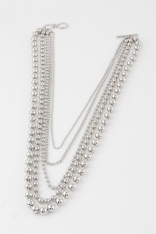 Five strand long necklace made of rounded shiny silver metal beads with a toggle closure. Shown lying flat