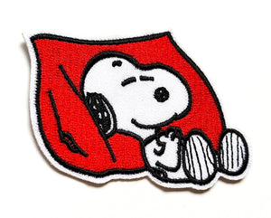 Black, white, and red embroidered patch of Snoopy sleeping against a big red pillow