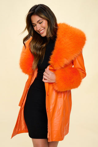 Model wearing orange faux fur trench coat with oversized orange faux fur shawl collar and wide cuffs. Shown open