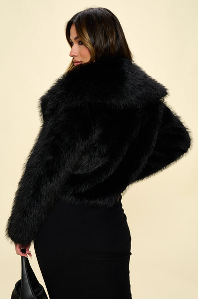 Model wearing a cropped black faux fur jacket with a shawl collar. Shown from back