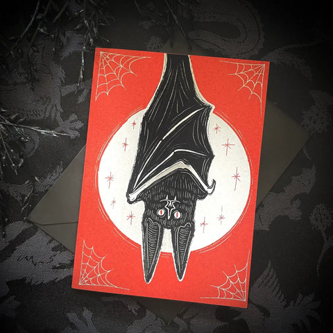 Note card featuring illustration of an upside down vampire bat in front of a full moon background with stars and spiderwebs