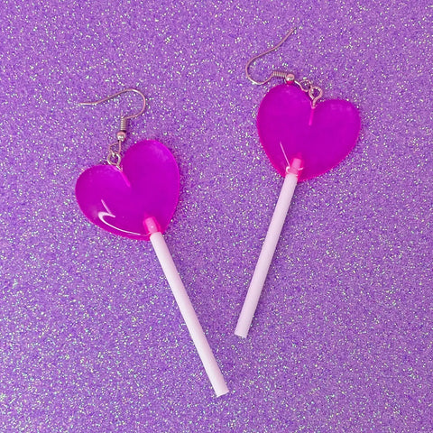 Pink acrylic heart-shaped lollipop earrings on white sticks on a pink glitter background
