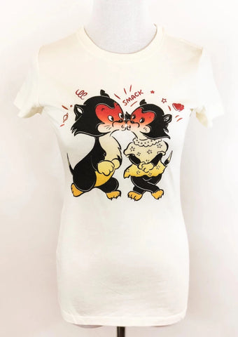 Warm off-white fitted cotton t-shirt with a vintage valentine style illustration of a pair of black and white cats with red blushing faces  surrounded by hearts, lines, and “SMACK” as onomatopoeia. Shown on a dress form