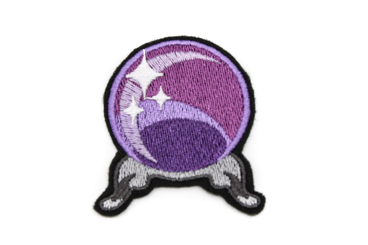 Embroidered patch of a crystal ball in three shades of purple with three stars pictured inside it in front of a crescent moon. Black felt border