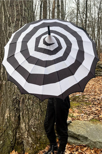 Model holding a black and white spiral patterned pagoda style umbrella open. Shown from the front 