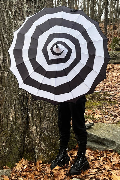 Model holding a black and white spiral patterned pagoda style umbrella open. Shown from the front held directly in front of model