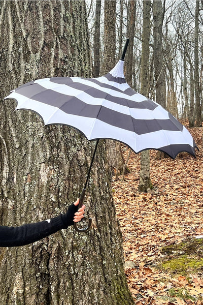 Model holding a black and white spiral patterned pagoda style umbrella open. Shown from the side