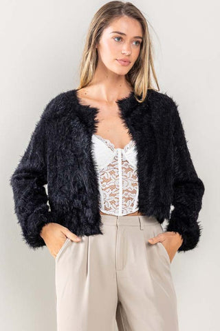Model wearing a cropped long sleeve open cardigan made of black faux-mohair fuzzy fabric. Shown from the front