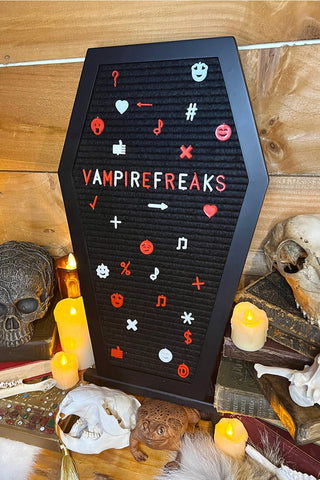 Black coffin shaped letter board with felt compartments. Orange and white letters spelling “VAMPIREFREAKS” surrounded by emojis and symbols. On a matching black easel 