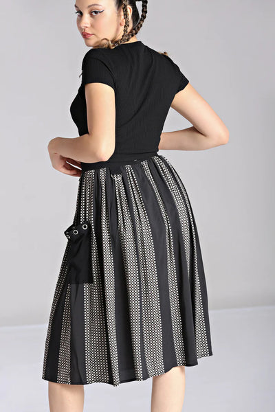A model wearing a midi length skirt in a black and grey check plaid with alternating black vertical stripes. It has a self waistband with silver metal D-ring detail at the left hip and large black patch pockets with silver metal grommets at the hem of the pockets. Shown from the back