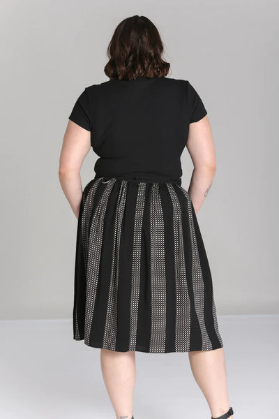 A plus size model wearing a midi length skirt in a black and grey check plaid with alternating black vertical stripes. It has a self waistband with silver metal D-ring detail at the left hip and large black patch pockets with silver metal grommets at the hem of the pockets. Shown from the back
