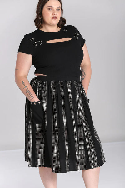 A plus size model wearing a midi length skirt in a black and grey check plaid with alternating black vertical stripes. It has a self waistband with silver metal D-ring detail at the left hip and large black patch pockets with silver metal grommets at the hem of the pockets. Shown from the front