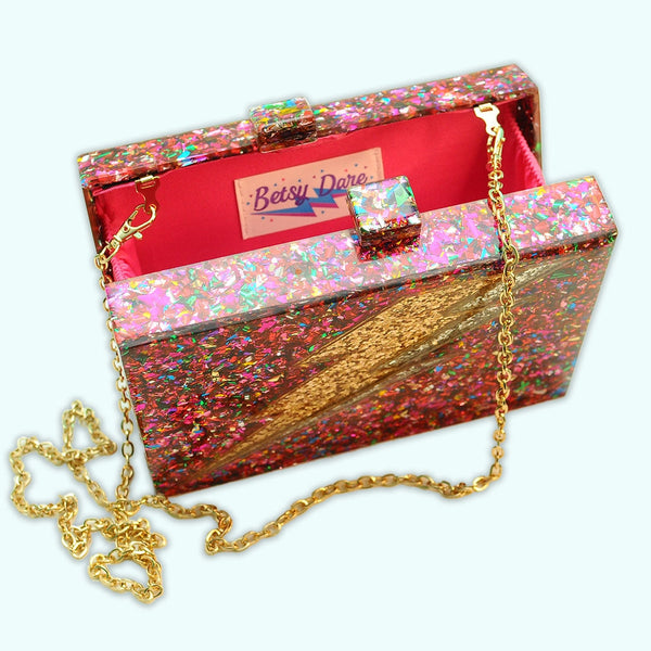 Rectangular hard resin clutch purse with chunky rainbow confetti inlaid. Large silver and gold glitter lightning bolt on front. Shown from the top open with chain strap
