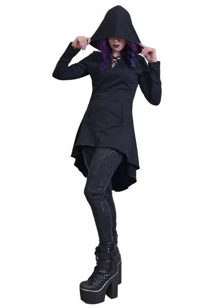 Model wearing black French Terry hoodie with feature neckline, long sleeves with thumb holes, a kangaroo pocket, oversized black hood (shown up), and a flared high-low hemline. Shown in full length shot from 3/4 angle to display hemline