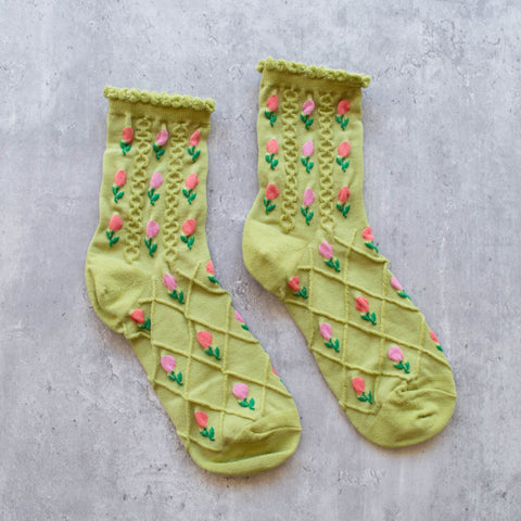 Bright green cotton knit socks with a textured wavy pattern and knit-in pattern of pink and purple tulips and ruffled cuffs. Shown lying flat