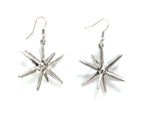 A pair of three dimensional starburst dangle earrings made of silver metal with a burnished finish