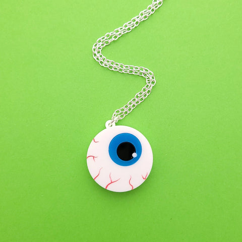 Laser-cut acrylic brooch of a cartoony bloodshot eyeball with bright blue iris on an 18” silver plated link style chain. Shown flat