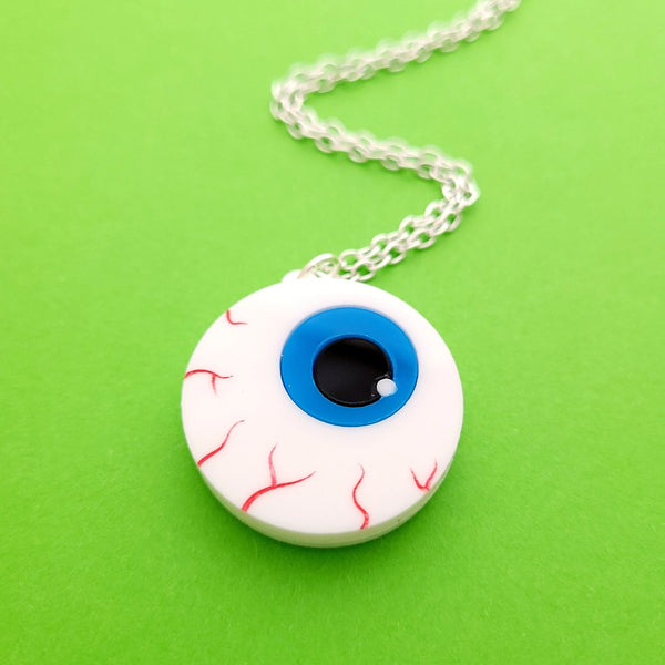Laser-cut acrylic brooch of a cartoony bloodshot eyeball with bright blue iris on an 18” silver plated link style chain. Shown flat up close
