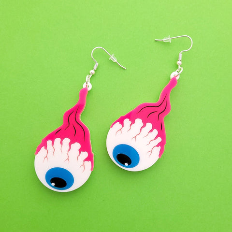 A pair of laser-cut acrylic dangle earrings of a pair of cartoony bloodshot eyeballs with blue irises hanging from bright pink optic nerves. Shown flat