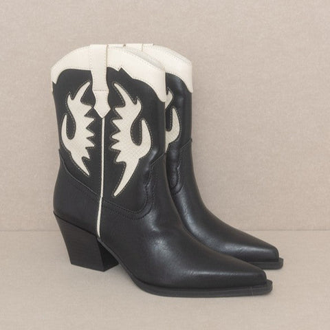 A pair of black pointed toe western style boots with pointed toes and 2” block heels. Black shiny faux leather with creamy white inset details. Shown from a three quarter angle 