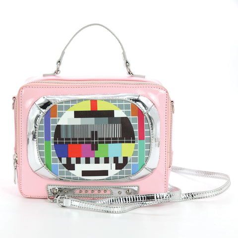 A rectangular novelty purse in the shape of a vintage television set in shiny pastel pink vinyl with silver details. Has a “screen” with a colorful test pattern and faux knob controls. Has a silver handle and detachable matching cross body strap. Shown from the front