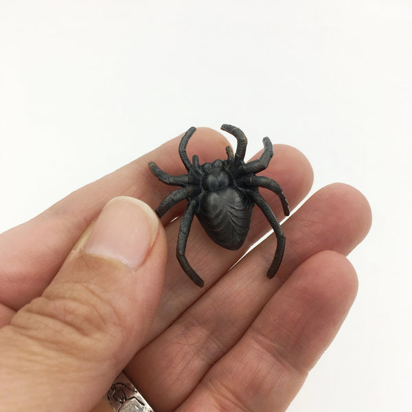 Black spider shaped brooch made of brass with oxidized shiny finish, held in a hand to show size
