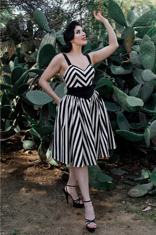 A model wearing a playsuit and skirt set made of stretch black and white cotton. The playsuit has a sweetheart neckline, princess seaming, and wide black adjustable straps. The skirt is a just below the knee swing skirt with a solid black yoke style waistband. Shown from the front 