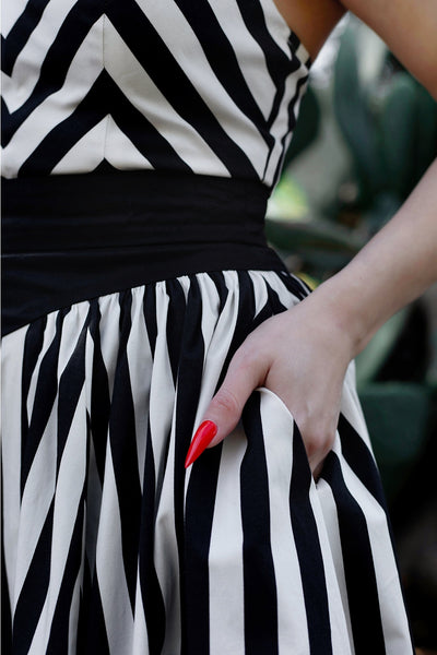 A model wearing a playsuit and skirt set made of stretch black and white cotton. The playsuit has a sweetheart neckline, princess seaming, and wide black adjustable straps. The skirt is a just below the knee swing skirt with a solid black yoke style waistband. Shown in close up of the skirt
