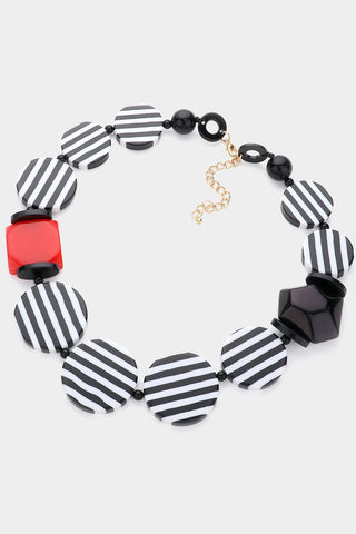 Necklace made of large flat black and white striped beads alternated with small round black beads and one bright red square bead with beveled black bead. Shown flat