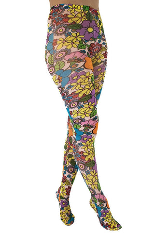 A model wearing tights printed with an all-over pattern of retro illustrations of multicolored yellow, purple, blue, green, red, and pink flowers with black outlines on a pale blush pink background. Shown from a three quarter angle